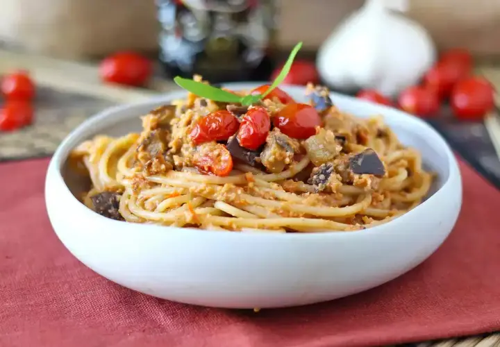 Un piatto invitante di pasta e melanzane alla napoletana, condito con pomodorini freschi e basilico.