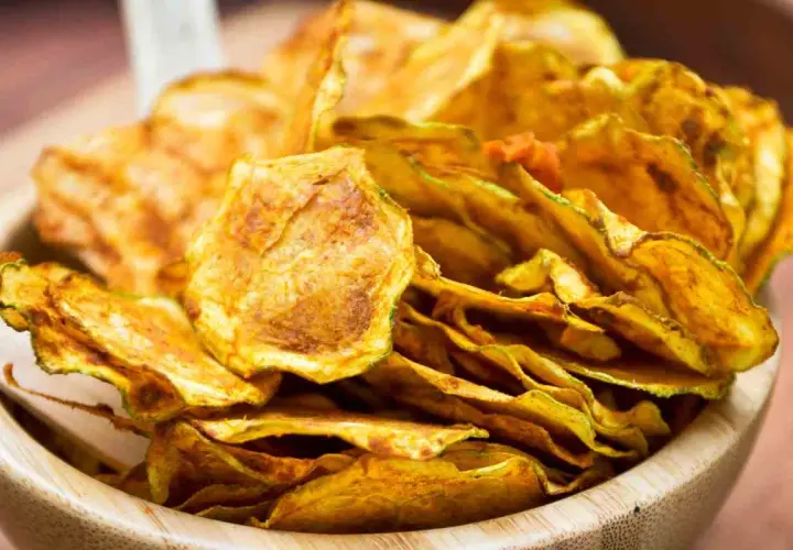 Croccanti chips di zucchine dorate, un'alternativa salutare e gustosa alle patatine, servite in una ciotola di legno.