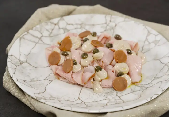Vitello tonnato ricetta: fettine rosa di vitello, salsa tonnata, capperi e acciughe su piatto di marmo.