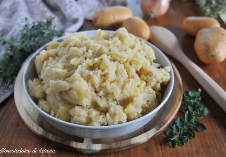 Patate in tecia, un contorno rustico e saporito, servito in una ciotola bianca su un tagliere di legno, con patate crude e erbe aromatiche sullo sfondo.