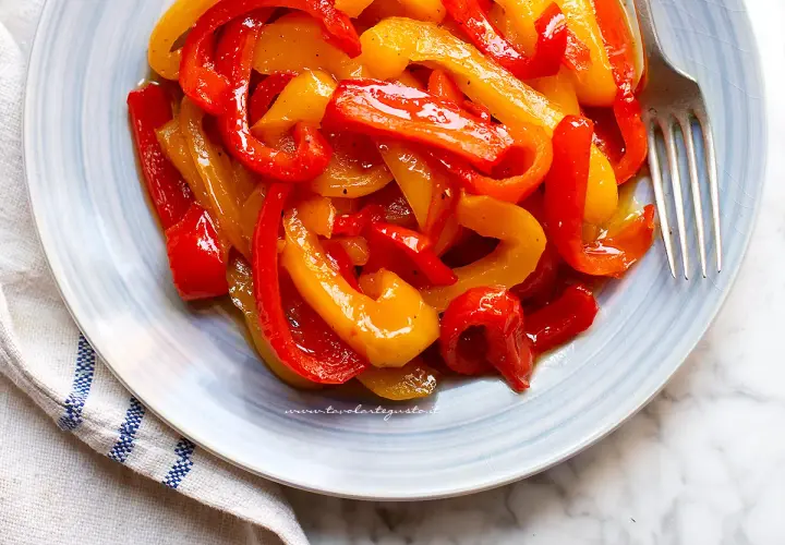 Piatto di peperoni in agrodolce, rossi e gialli, conditi con olio e spezie, pronti per essere gustati.