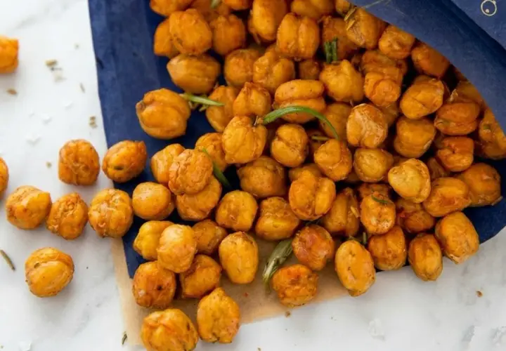 Ceci croccanti al forno, dorati e speziati, versati da un sacchetto blu. Perfetti per uno snack salutare.