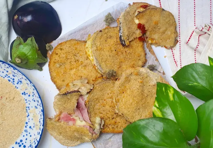Cordon bleu di melanzane impanati e fritti, ripieni di prosciutto e formaggio filante. Accanto, melanzane fresche e pangrattato.