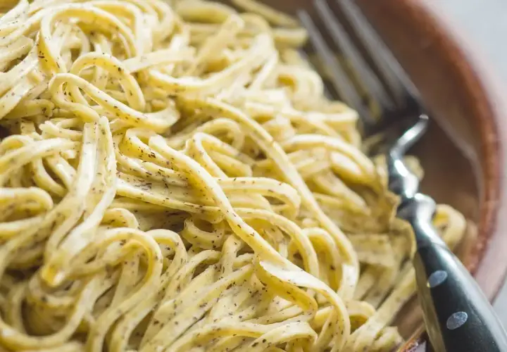 Un primo piatto invitante: tagliolini al limone, conditi con una crema delicata e erbe aromatiche, pronti per essere gustati con una forchetta.