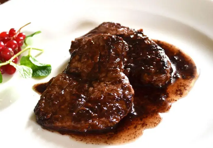 Tre fette di brasato di manzo succulento in salsa scura, guarnite con ribes rossi e menta fresca.