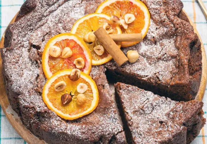 Deliziosa torta di pane al cioccolato, cosparsa di zucchero a velo, decorata con fette d'arancia, nocciole e cannella.