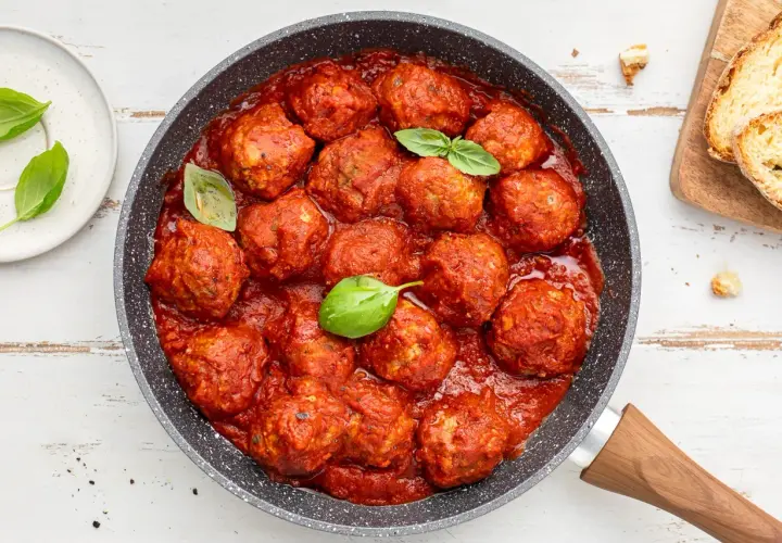 Succulente polpette di carne in padella, immerse in un ricco sugo di pomodoro, guarnite con foglie di basilico fresco.
