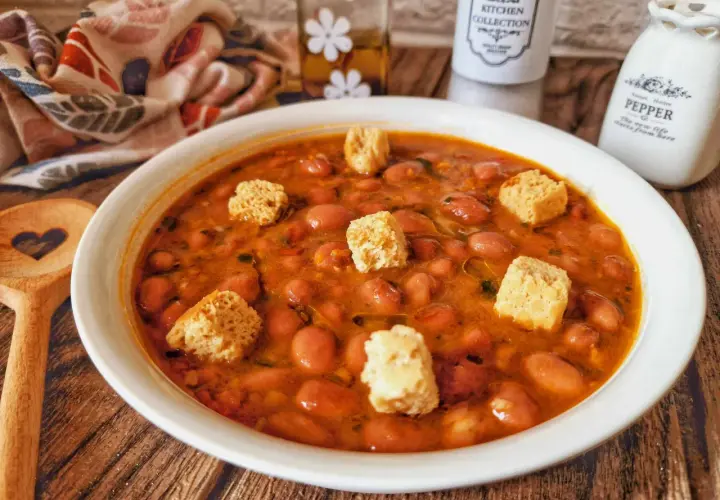 Una ciotola di zuppa di fagioli fumante, guarnita con crostini croccanti, pronta per essere gustata.