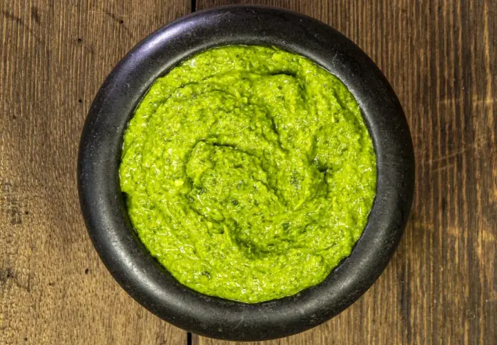 Un mortaio di pietra nera contiene un vibrante pesto alla genovese, pronto per condire la pasta.