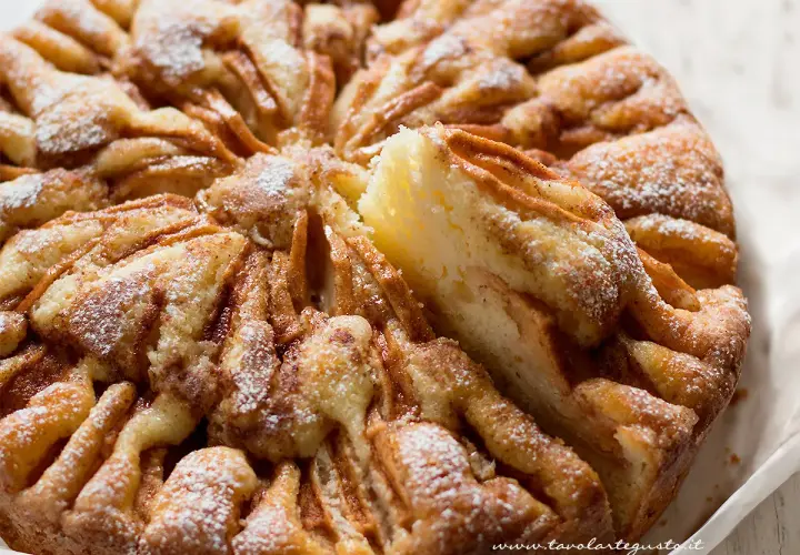 Una deliziosa torta di mele, con fette di mela disposte a raggiera e spolverata di zucchero a velo.