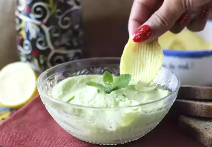 Una mano intinge una patatina in una cremosa maionese con uovo sodo, guarnita con menta.