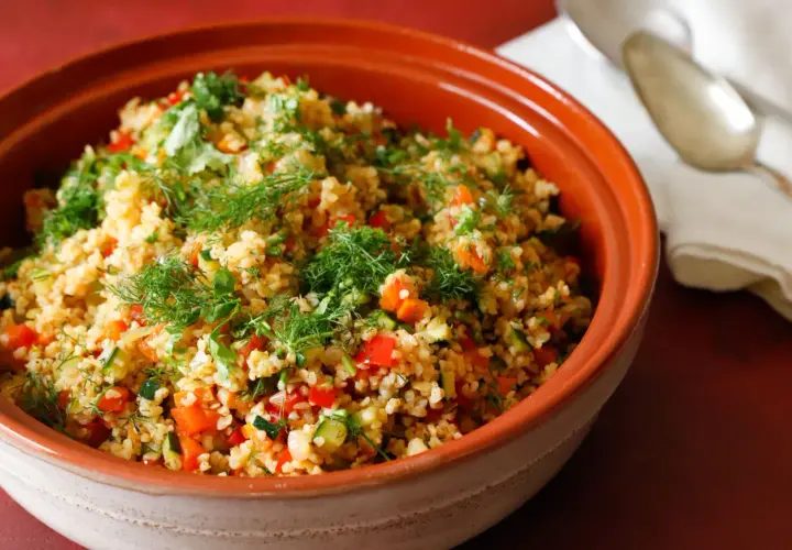 Tabulè di verdure fresco e colorato, con pomodori, zucchine e erbe aromatiche, servito in una ciotola di terracotta.