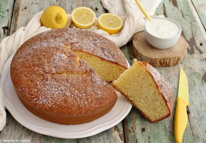 Deliziosa torta per colazione, soffice e profumata al limone, spolverata di zucchero a velo, con una fetta tagliata e una ciotolina di yogurt.