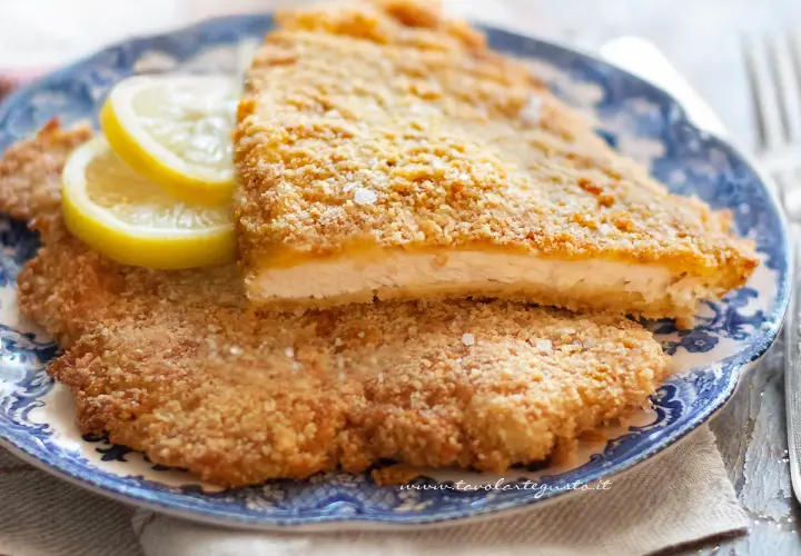 Due cotolette al forno dorate e croccanti, servite su un piatto blu con spicchi di limone.