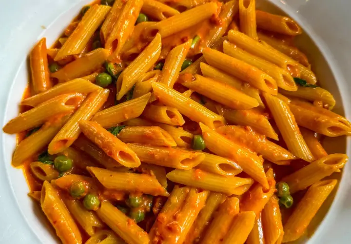 Penne ai 7 peccati, un piatto di pasta avvolto in una cremosa salsa rossa, con piselli verdi che spuntano come gemme preziose.