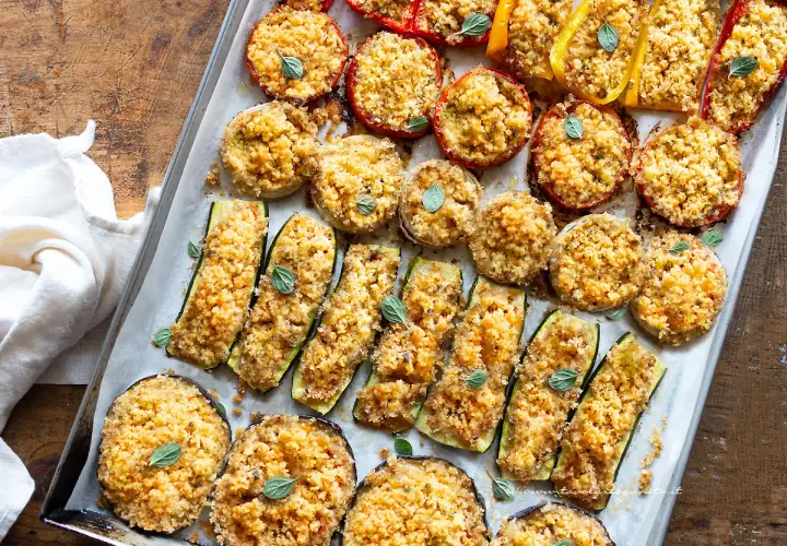 Verdure gratinate al forno: zucchine, melanzane, pomodori e peperoni ripieni di pangrattato e erbe aromatiche, cotti su una teglia.
