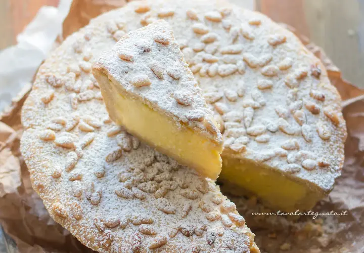 Torta della nonna facile, con crema gialla, pinoli e zucchero a velo. Una fetta è stata tagliata.
