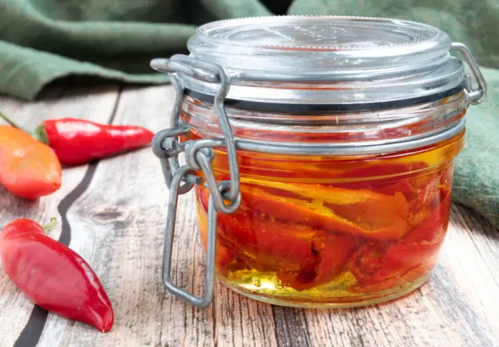 Barattolo di **olio al peperoncino** fatto in casa, con peperoncini rossi freschi accanto su un tavolo di legno.