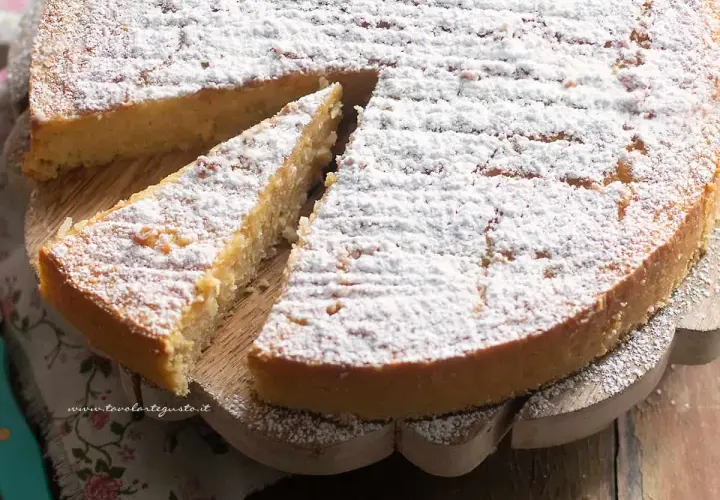 Una fetta di torta di riso, cosparsa di zucchero a velo, attende di essere gustata su un tagliere di legno.