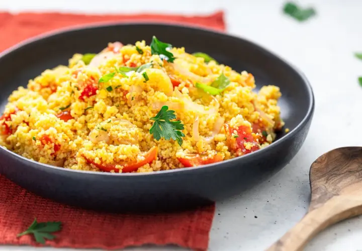 Un piatto invitante di cous cous freddo con pomodorini, cipolle e prezzemolo fresco. Perfetto per un pasto leggero e saporito.