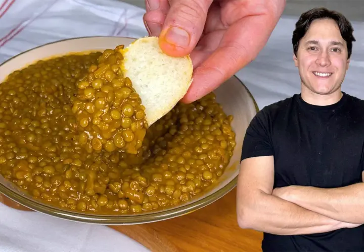 Un uomo sorride mentre un pezzo di pane intinge un piatto di saporite lenticchie in umido.