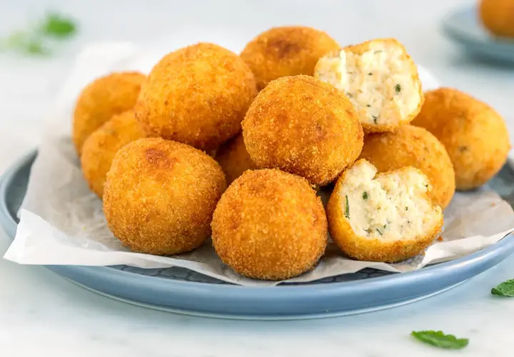 Un piatto di polpette di ricotta dorate e croccanti, alcune intere, altre spezzate per mostrare il ripieno morbido e profumato.