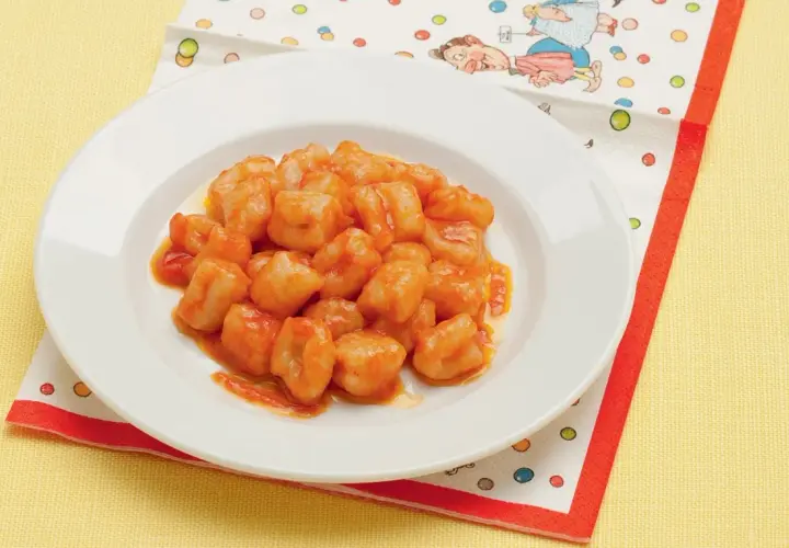 Un piatto di chicche di patate condite con un sugo rosso, servite su un tovagliolo colorato.