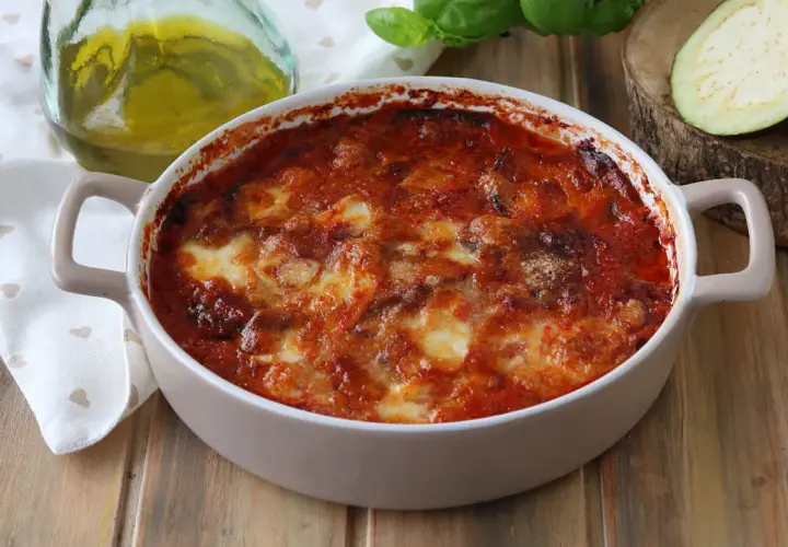 Parmigiana di melanzane appena sfornata, dorata e filante, con pomodoro e basilico fresco.