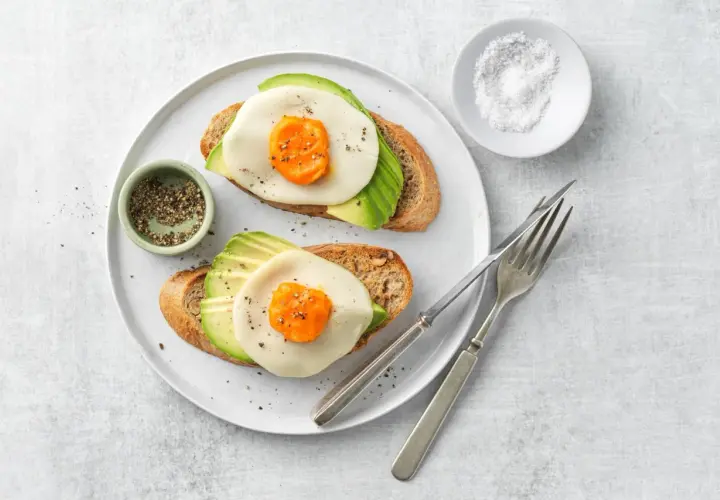 Due fette di pane tostato con avocado, formaggio e un occhio di bue, condite con pepe.