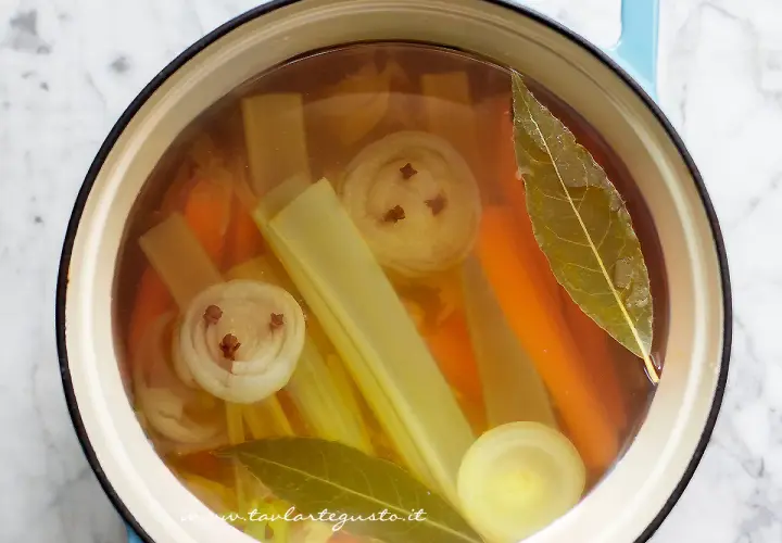 Brodo vegetale ricetta: carote, sedano, cipolla con chiodi di garofano e alloro in pentola.