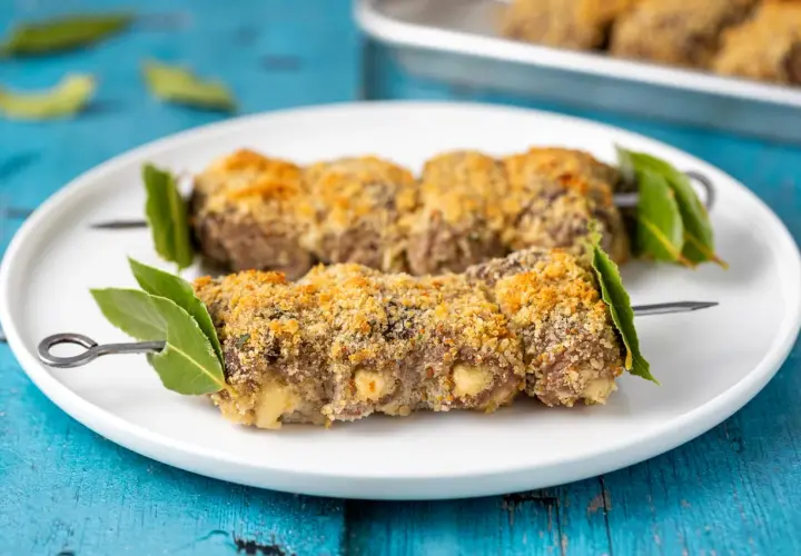 Braciole alla messinese su spiedini, impanate e dorate, guarnite con foglie di alloro.