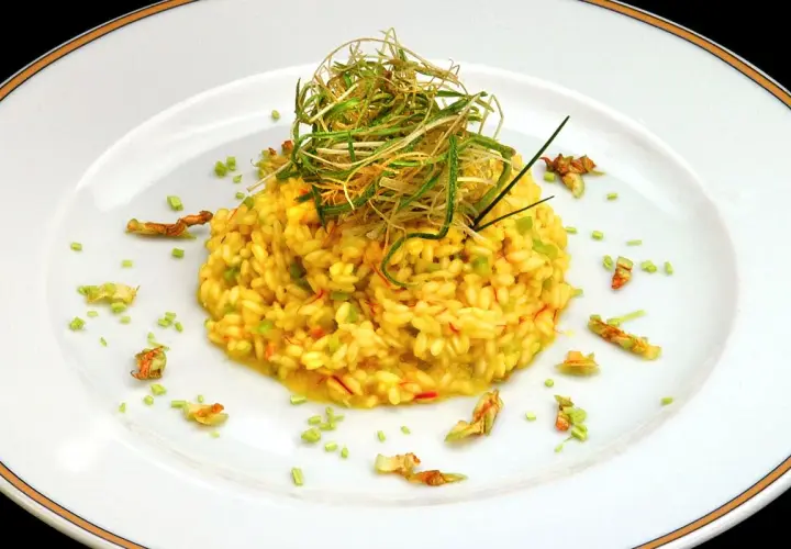 Risotto giallo intenso con fiori di zucca e zafferano, guarnito con erbe croccanti.