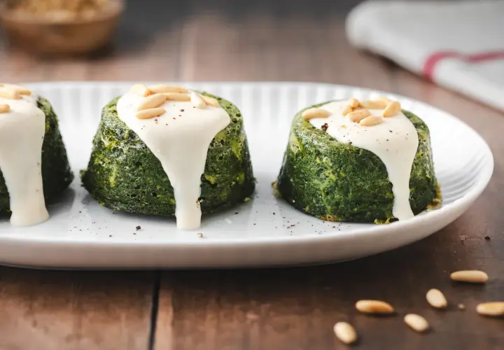 Delizioso flan di verdure servito su un piatto bianco, guarnito con salsa cremosa e pinoli tostati.