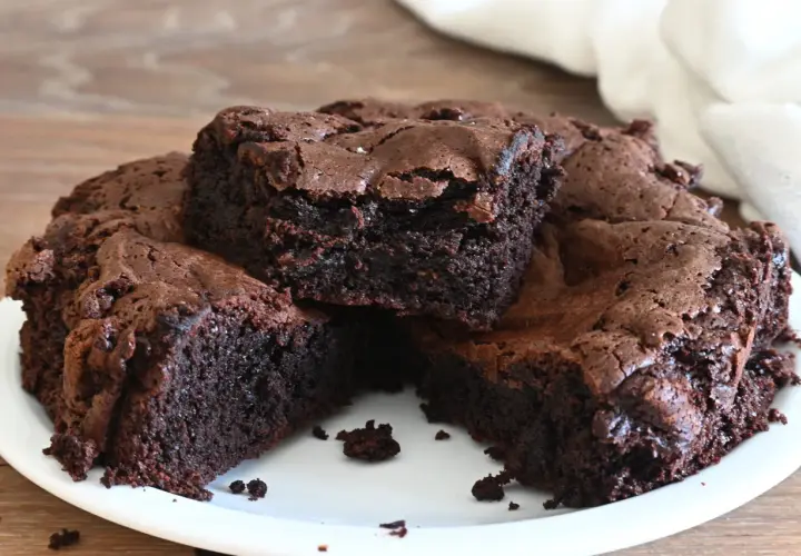 Torta al cioccolato, soffice e umida, tagliata a fette su un piatto bianco. La crosta è leggermente screpolata, rivelando l'interno scuro e invitante.
