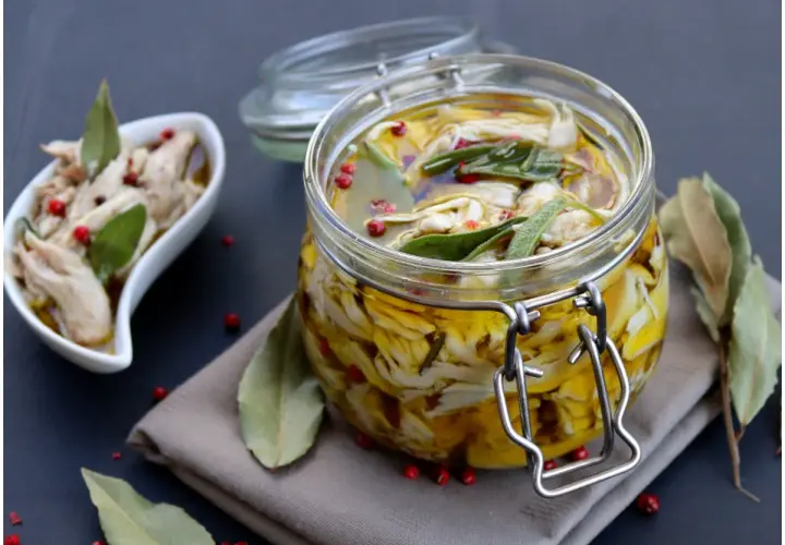 Tonno di coniglio sott'olio, sfilacciato e conservato in un barattolo di vetro con erbe aromatiche e pepe rosa.