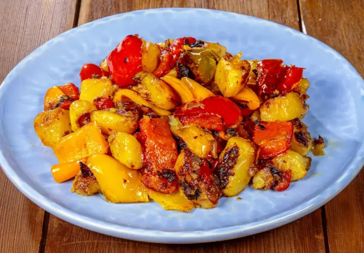 Pipi e patate arrostiti, un contorno colorato e saporito, servito su un piatto azzurro.