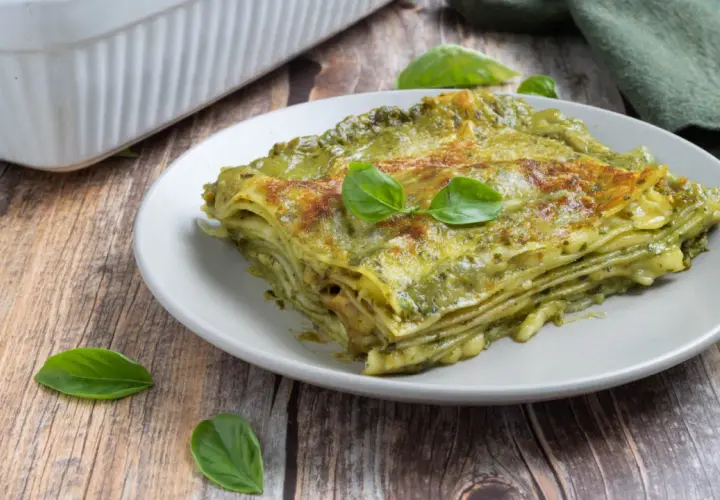 Una fetta di lasagne al pesto, stratificata e dorata, guarnita con basilico fresco su un piatto grigio.