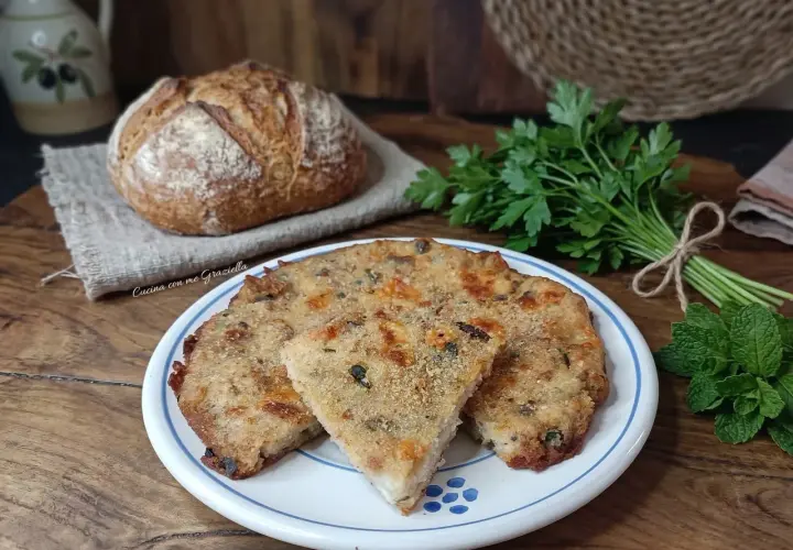 Frittata di pane dorata e saporita, servita su un piatto bianco con bordi blu, accanto a pane fresco e erbe aromatiche.