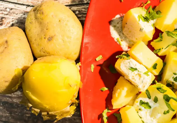 Patate fresche e un'appetitosa insalata di patate condita con erbe aromatiche su un piatto rosso.