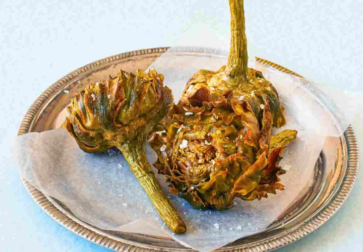 Due carciofi alla giudia dorati e croccanti, cosparsi di sale grosso, su un vassoio d'argento.