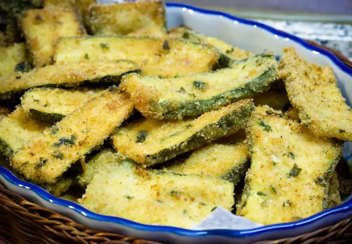 Fettine di zucchine impanate e dorate, appena tolte dalla padella, servite in una ciotola.