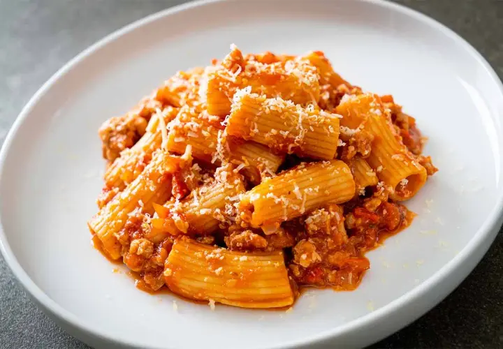 Un piatto di pasta alla zozzona, con rigatoni conditi con un ricco ragù di carne e abbondante parmigiano grattugiato.