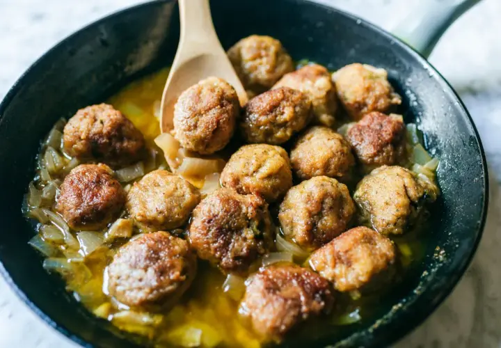Polpette in bianco succulente in padella con cipolle caramellate, pronte per essere gustate.