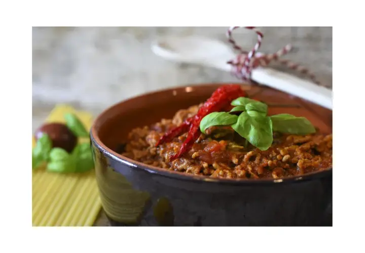 Un saporito ragù di verdure, guarnito con peperoncino e basilico, in una ciotola di terracotta.