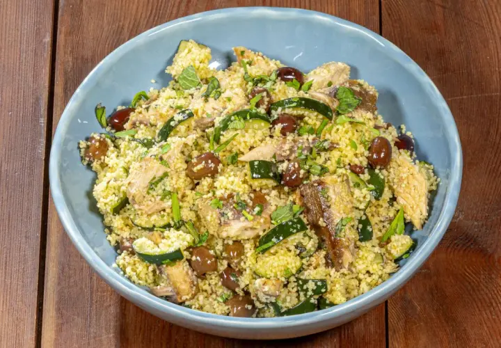 Un saporito cous cous con verdure, olive e pesce, guarnito con erbe fresche.