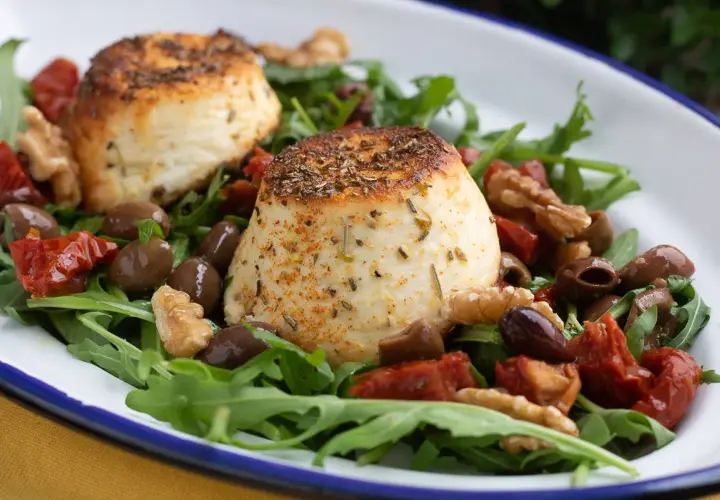 Due dischi di ricotta al forno su un letto di rucola, pomodori secchi, olive e noci.