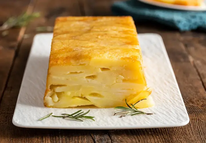 Sformato di patate a fette dorato e invitante, servito su un piatto bianco con rametti di rosmarino.