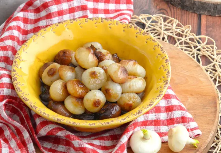 Cipolline in agrodolce caramellate in una ciotola gialla, servite su un tagliere di legno con tovagliolo a quadri rossi.