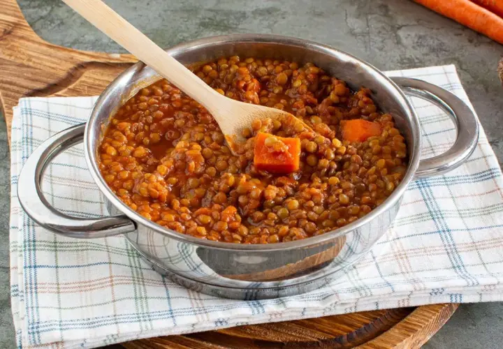 Un pentolino pieno di saporito ragù di lenticchie, con pezzi di carota e un cucchiaio di legno.