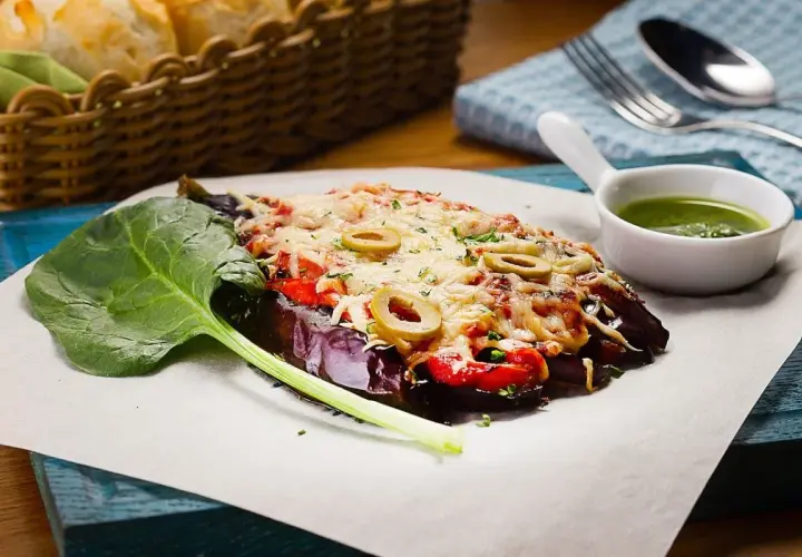Caponata di melanzane gratinata con olive, pomodoro e formaggio fuso, servita con spinaci freschi e salsa verde.